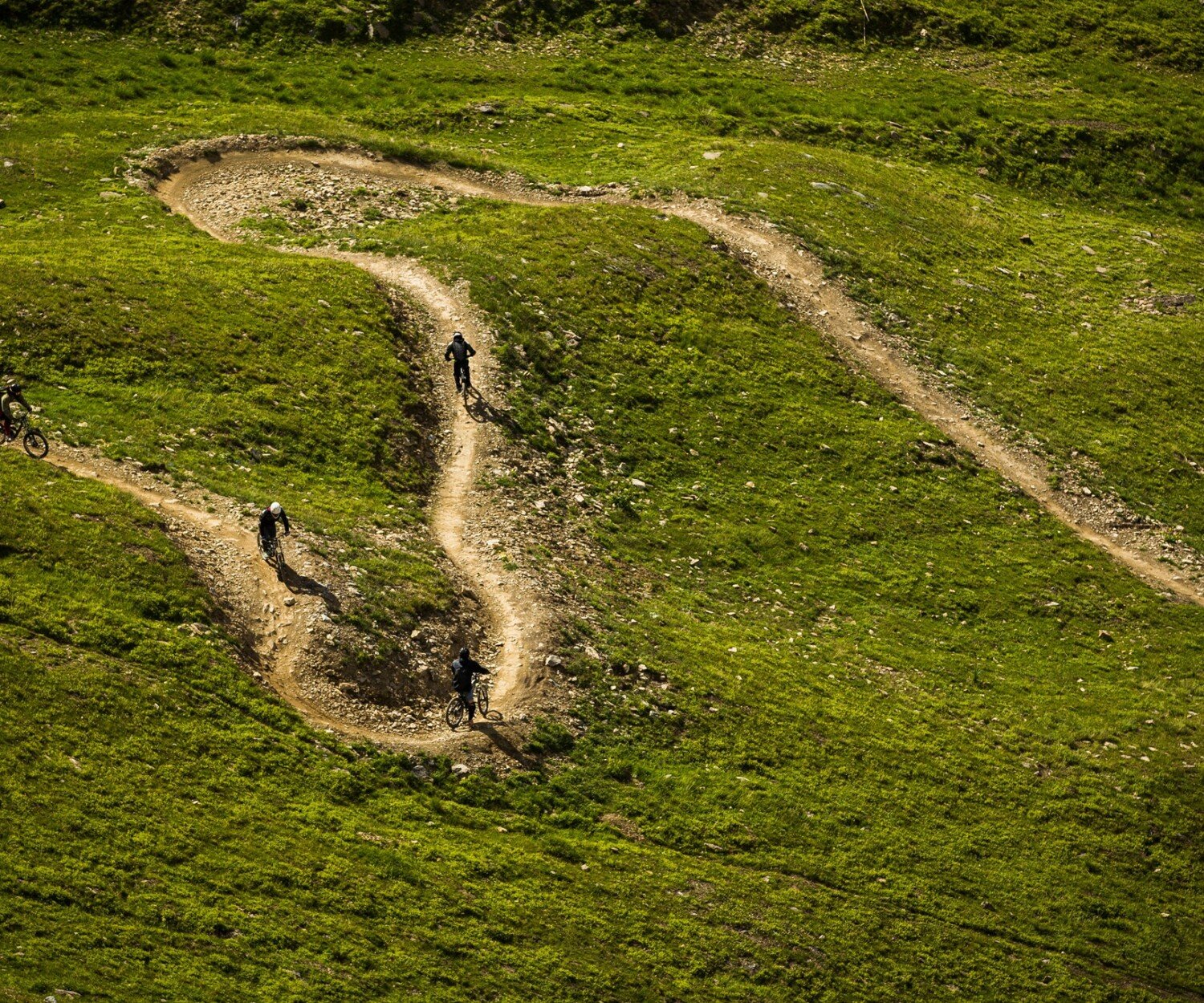 Mountain Bikers riding a singletrack with berms in the Bike Park and Les Deux Alpes, France.